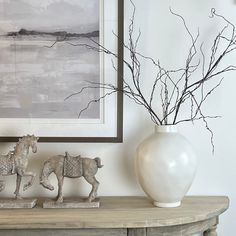 a white vase sitting on top of a wooden table next to a painting and figurines