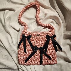 a pink purse with black bows on the handle and straps, sitting on a bed