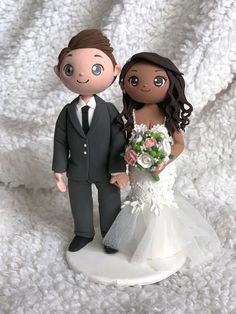 a wedding cake topper with a bride and groom standing next to each other on a white blanket