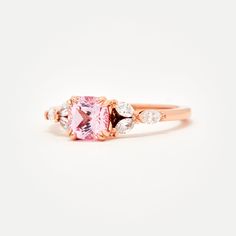 Custom designed by Amelie, and exclusive to Identity Diamonds Recycled metal Set in the center with a lovely 1.25ct* (6mm) cushion cut lab-grown rosé sapphire With a blush hue reminiscent of the color of morganite, our rosé sapphire features a slightly more saturated pink, and it offers a much better durability than morganite, making it ideal for an engagement ring! Available in two different tones: a hint of peach, or a hint of lavender in it Features six marquise shaped lab-grown diamonds, for Rose Gold Cushion Cut Ring With Accent Stones, Rose Gold Square Cut Promise Ring, Rose Gold Rings With Asscher Cut And Accent Stones, Rose Gold Square Cut Fine Jewelry Ring, Luxury Rose Gold Square Cut Ring, Rose Gold Square Cut Wedding Rings, Spinel Engagement Rings, Montana Sapphire Engagement, Montana Sapphire Engagement Ring