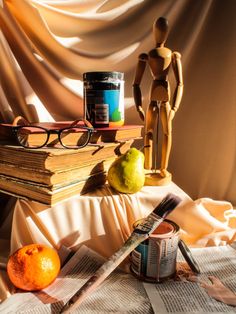 a table topped with books and an orange next to a pair of eyeglasses