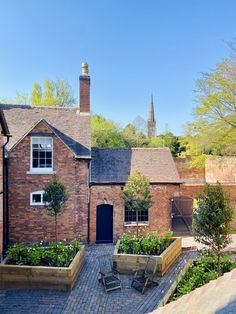 a brick house with an outdoor garden and seating area in the foreground, on a sunny day