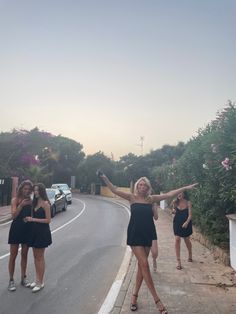 three women standing on the side of a road pointing at something in the air with their arms outstretched