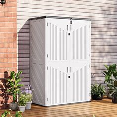 a white storage shed sitting on top of a wooden deck next to potted plants