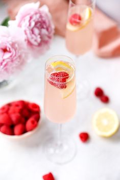 two glasses filled with pink lemonade and raspberries on a table next to flowers