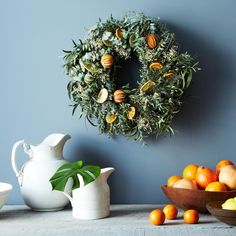 a wreath is hanging on the wall next to bowls of fruit and a bowl of oranges