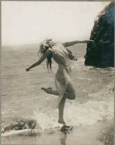 a woman standing on top of a wave covered beach next to the ocean with her arms outstretched