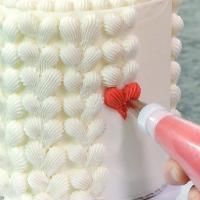 someone is painting the side of a cake with white frosting and red decorations on it