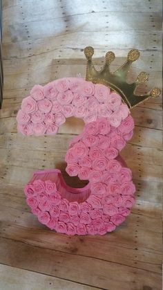 the number three made out of pink roses with a crown on top is displayed in front of a wooden background