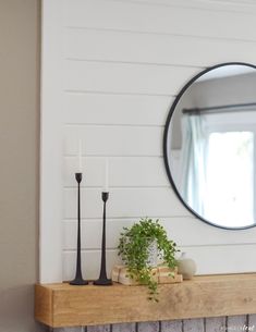 a mirror on the wall above a mantle with candles and a potted plant next to it