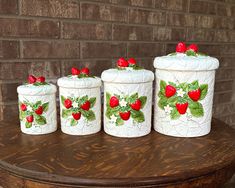 four ceramic containers with strawberries on them sitting on a table next to a brick wall