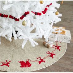 a white christmas tree decorated with red and gold ornaments on a round rug in a living room