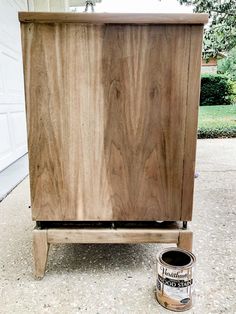 a wooden cabinet sitting on top of a cement ground next to a can of paint