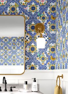 a bathroom with blue and yellow tiles on the wall, gold faucet and mirror