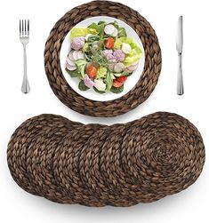 a white plate topped with salad next to a woven placemat and silverware set on top of a table