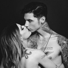 a man and woman kissing each other with tattoos on their chests, in black and white