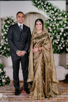 a man and woman standing next to each other in front of a wedding arch with flowers