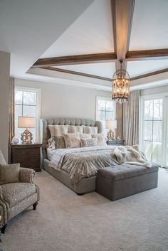 a bedroom with a large bed and chandelier hanging from the ceiling in front of two windows