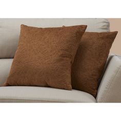 two brown pillows sitting on top of a couch next to a white pillow case and a beige chair