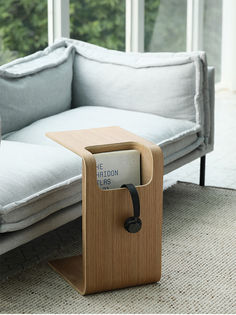 a couch with a book holder on it in front of a window and some pillows