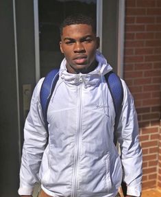 a man standing in front of a building wearing a white jacket and khaki pants