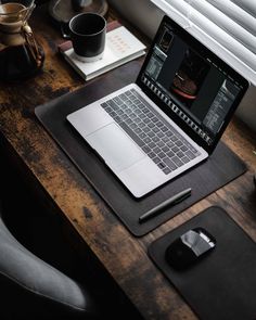 an open laptop computer sitting on top of a wooden desk next to a cup of coffee