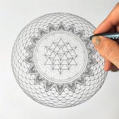 a person is drawing a flower of life on a white paper with a marker and pen