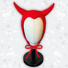 a red knitted hat with horns on top of a black stand against a white background