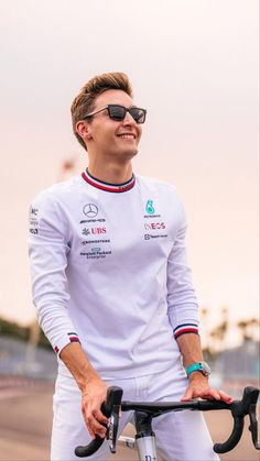 a man in white is standing next to his bike wearing sunglasses and holding the handlebars