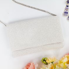 a white purse sitting on top of a table next to flowers