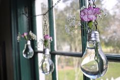 three light bulbs hanging from the side of a window with flowers in them and one bulb attached to it