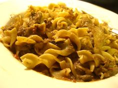 a white plate topped with pasta and meat covered in gravy next to a fork