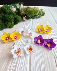 four flower earrings sitting on top of a white table next to broccoli and moss