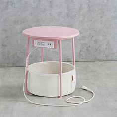 a pink table with a white basket underneath it and an electrical outlet plugged in