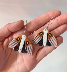 a pair of earrings in the palm of someone's hand, with an orange and black butterfly on it