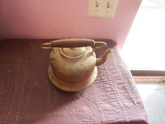 an old brass tea pot sitting on top of a purple table cloth next to a light switch