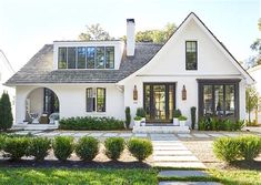 a white house with lots of windows and bushes in front of the door is surrounded by greenery