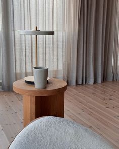 a small table with a lamp on it in front of a curtained room window