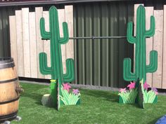 two fake cactus stands in the grass next to a barrel