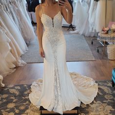 a woman taking a selfie in front of her wedding gowns at the bridal shop