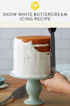 a person holding a knife over a cake on a plate with the words snow white buttercream icing recipe