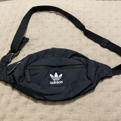 an adidas fanny bag laying on top of a bed next to a black strap