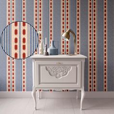 a white table sitting next to a wall with a mirror on top of it in front of a blue and red striped wallpaper