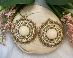 a pair of beaded earrings sitting on top of a piece of wood next to flowers