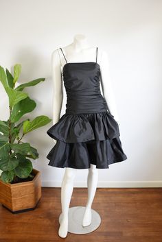 "Description: Black party dress with a drop waist and ruffled skirt. zips up the back and has a large decorative bow. Some tulle under the skirt for fullness.  Bodice has boning up the sides.  Measurements of garment, allow space for fit.  Bust: 32\" has some gathers for cup space. Shown on 36\" and it was way too snug. Waist: 28\" Hips: Open Length: 37\" Skirt length: 15\" I take my measurements flat, and double for circumference.    Tag: No brand, just an ILGWU label.   Fabric: Polyester Condition:  Excellent" Party Dress With Ruffle Hem And Fitted Bodice, Party Dress With Ruffle Hem And Tiered Skirt, Fitted Party Dress With Gathered Skirt, Party Mini Dress With Ruffle Hem And Fitted Bodice, Fitted Dress With Gathered Skirt For Party, Evening Tiered Mini Dress With Ruffle Hem, Party Dresses With Ruffle Hem And Tiered Shape, Voluminous Ruffled Mini Dress For Cocktail, Tiered Ruched Party Dress