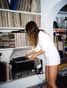 a woman in white shirt and shorts playing with an old fashioned record player on top of a shelf