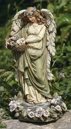 a statue of an angel holding a basket of flowers on a rock in the grass