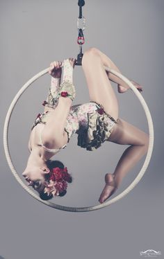 a woman is suspended upside down in a hoop with flowers on her body and legs