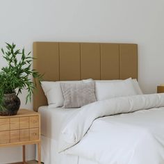 a bed with white sheets and pillows next to a wooden nightstand holding a potted plant