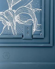 a light switch is shown in front of a blue wall with an artistic painting on it